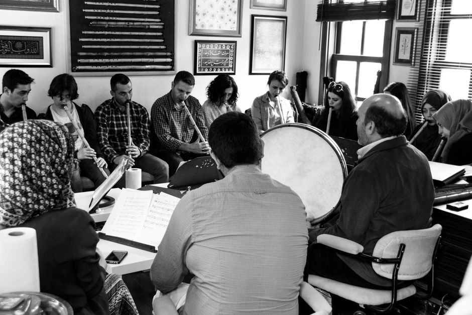 A diverse group of adults in a music class playing various instruments indoors.